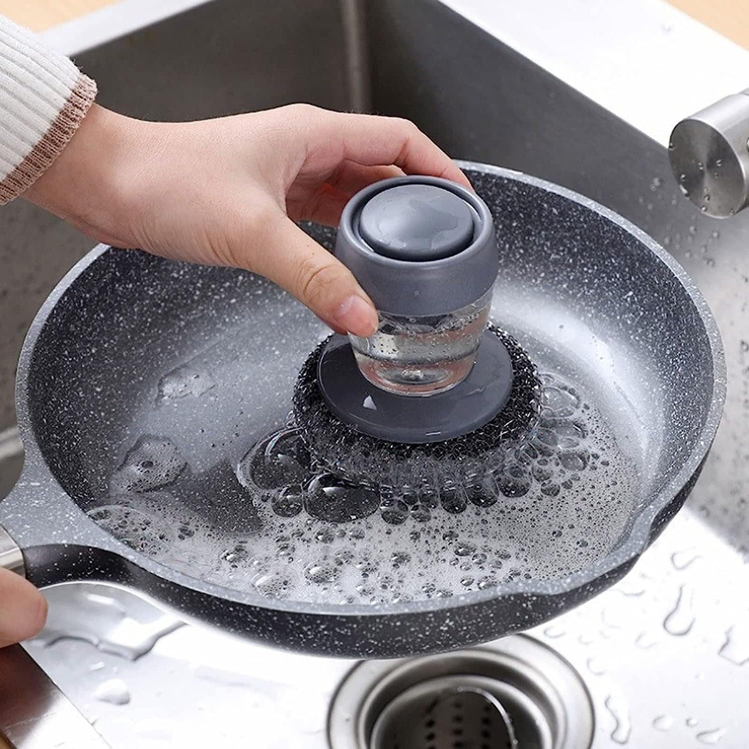 Hand using a soap dispensing palm scrubber to clean a pan